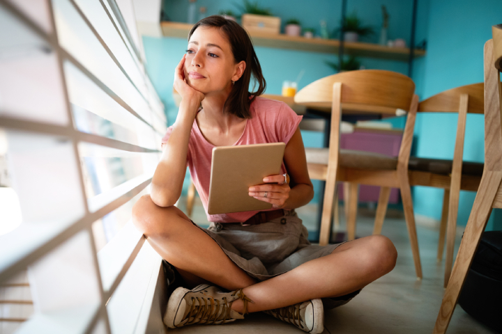 A woman sitting on the floor with her tablet, considering abortion as an option for her pregnancy.